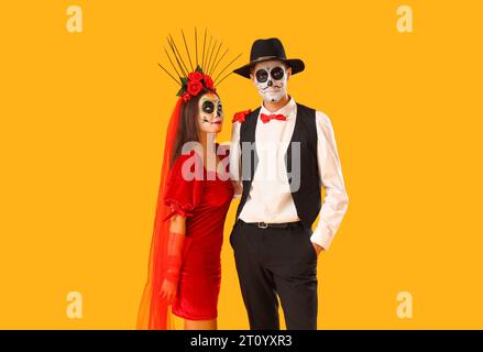 Junges Paar, das für Mexikos Tag der Toten (El Dia de Muertos) auf gelbem Hintergrund gekleidet ist Stockfoto
