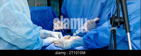Hände von Ärzten und Krankenschwestern in sterilen Handschuhen führen eine Operation in der Notaufnahme eines Krankenhauses durch. Chirurgen operieren mit chirurgischen Instrumenten. Stockfoto