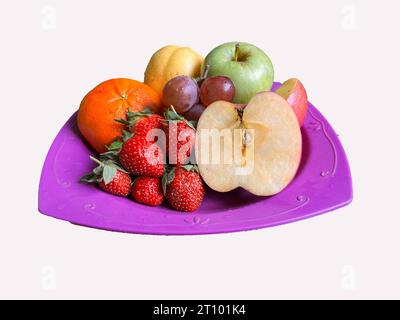 Erdbeeren, Äpfel, Orangen, Trauben, Birnen serviert auf einem lila Teller Stockfoto