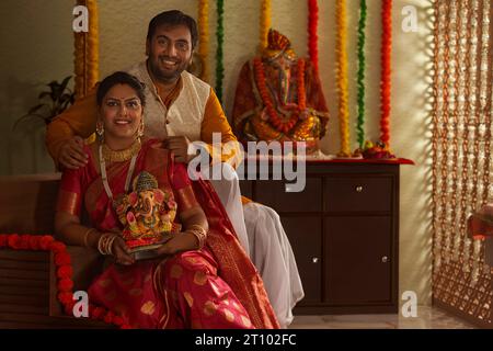 Ein junges Maharashtrianpaar, das ein Idol von Lord Ganesha hält, während er zusammen auf der Treppe sitzt Stockfoto
