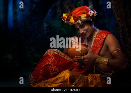 Junger Mann verkleidet als Lord Krishna isst Makhan anlässlich von Janmashtami Stockfoto