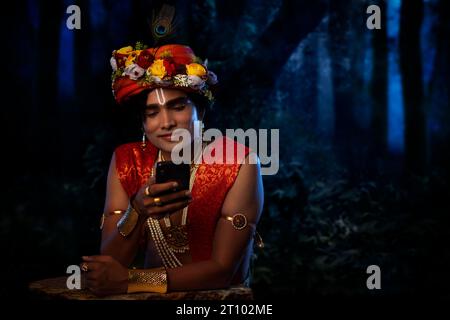 Junger Mann verkleidet als Lord Krishna und benutzt Handy Stockfoto