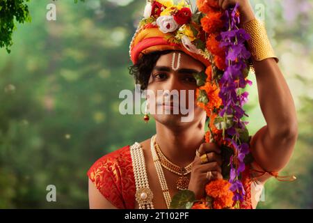 Porträt eines jungen Mannes, der als Lord Krishna verkleidet ist und anlässlich des Janmashtami auf einer Schaukel sitzt Stockfoto