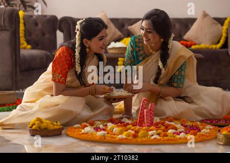 Südindische Frauen in weißem Saree dekorieren den Boden mit Blumen, um Onam zu feiern Stockfoto