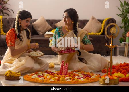 Südindische Frauen in weißem Saree dekorieren den Boden mit Blumen, um Onam zu feiern Stockfoto