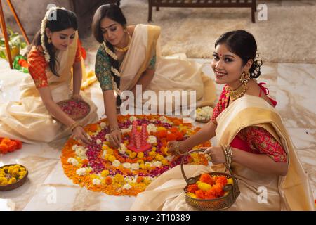 Südindische Frauen in traditioneller Kleidung schmücken den Boden mit Blumen zusammen, um Onam zu feiern Stockfoto