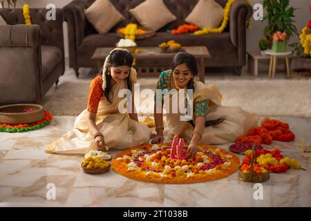 Südindische Frauen in weißem Saree dekorieren den Boden mit Blumen, um Onam zu feiern Stockfoto