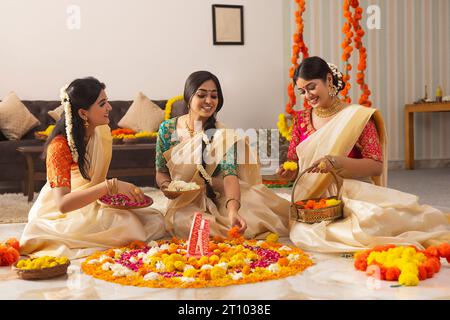 Südindische Frauen in weißem Saree dekorieren den Boden mit Blumen zusammen, um Onam zu feiern Stockfoto