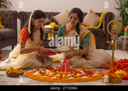 Südindische Frauen in weißem Saree dekorieren den Boden mit Blumen, um Onam zu feiern Stockfoto