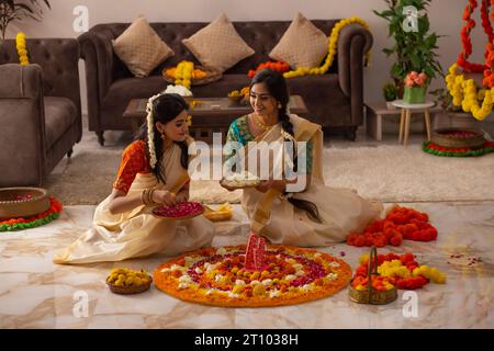 Südindische Frauen in weißem Saree dekorieren den Boden mit Blumen, um Onam zu feiern Stockfoto