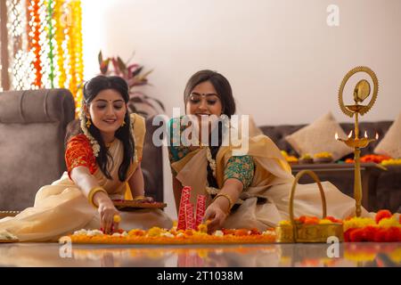 Südindische Frauen in weißem Saree dekorieren den Boden mit Blumen, um Onam zu feiern Stockfoto