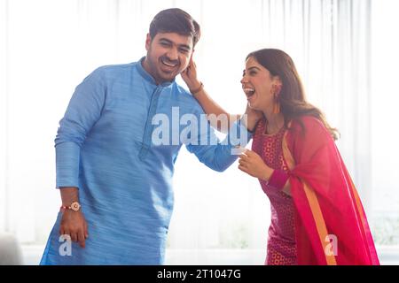 Geschwister ziehen sich liebevoll das Ohr, während sie Raksha Bandhan feiern Stockfoto