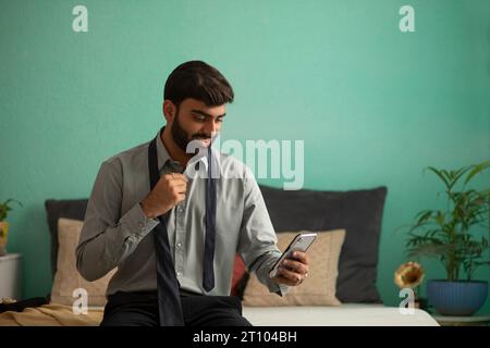 Junger Mann, der das Handy benutzt, während er sich anzieht Stockfoto