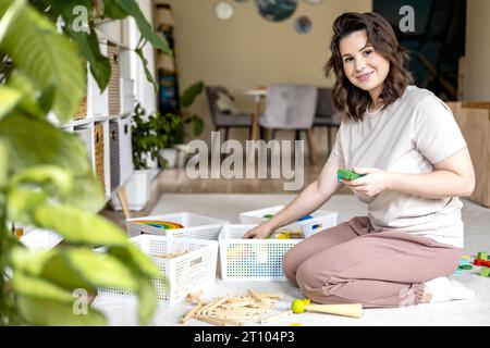 Lächelnde weibliche Hausfrau Kinderspielzeug Aufbewahrung organisiert Sortierdetails mit Korb PVC-Behälter Stockfoto