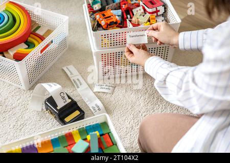 Frau reinigt kindliche Räume, sortiert Holz- und Plastikspielzeug, benutzt den Titel des mobilen Etikettendruckers Stockfoto
