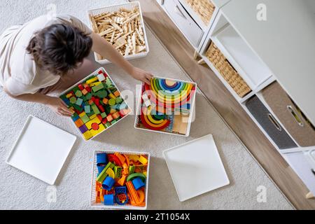 Junge Frau, die kindliches Spielzeug sortiert, Holz Montessori und Kunststoff Details Box Korb von oben Stockfoto