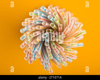 Überkopfansicht einer Gruppe farbiger Strohhalme, die eine Spirale auf gelbem Hintergrund bilden. Stockfoto