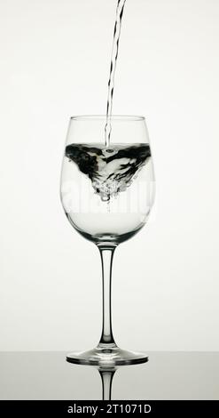 Ein Glas Wasser auf weißem Hintergrund mit einem Bach, der fällt und einen Wirbel bildet. Stockfoto