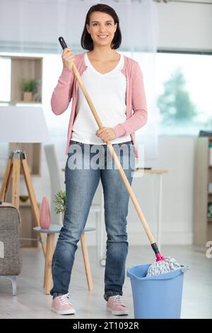 Eine Frau hält einen Mopp und reinigt den Wohnzimmerboden Stockfoto