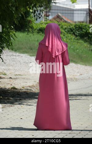 Muslimisches Mädchen in einem langen rosa Kleid und Kopftuch, von hinten gesehen. Stockfoto