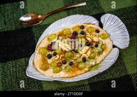 Haferbrei mit Früchten, Nüssen, Honig und Moringapulver in fischförmigem Deko-Teller auf karierter grüner Wolldecke mit Löffel. Stockfoto