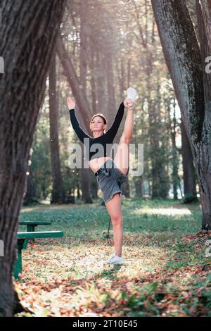 Eine Frau, die Yoga übt, führt die Übung Utthita Hasta Padangusthasana, eine Balance Asana, Training an einem sonnigen warmen Herbsttag im Park während St Stockfoto