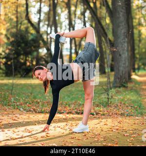 Eine Frau, die Yoga praktiziert, führt eine Variation der Ardha Chandrasana Übung durch, sichelförmige Haltung, Training, während sie an einem sonnigen warmen Herbsttag in t steht Stockfoto