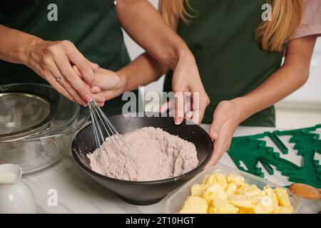 Mutter zeigt der Teenager-Tochter, wie man den Schneebesen benutzt, wenn man Kuchenzutaten miteinander mischt Stockfoto