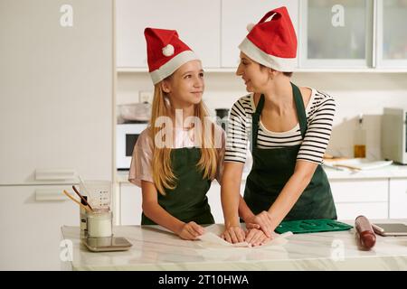 Glückliche Mutter und Tochter in Weihnachtsmannhüten, die Kekse zu Weihnachten machen Stockfoto