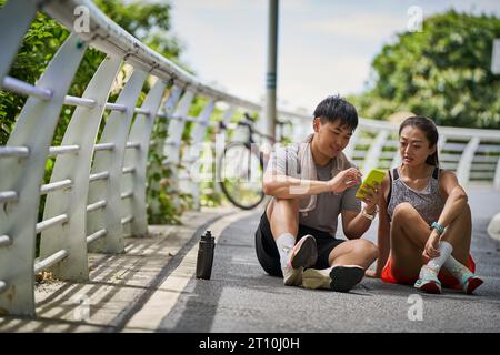 Junges asiatisches Paar teilt Handyfotos während einer Pause während des Trainings im Freien Stockfoto