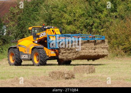 Der Teleskoplader JCB Agrisuper 532,60 mit einem Albutt F155A Heuballengreifer hebt zwei große 14 gebundene Ballen an und stellt ein Drittel zum Stapeln auf einem Anhänger auf. Stockfoto