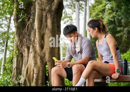 Junges asiatisches Paar teilt Handyfotos während einer Pause während des Trainings im Freien Stockfoto