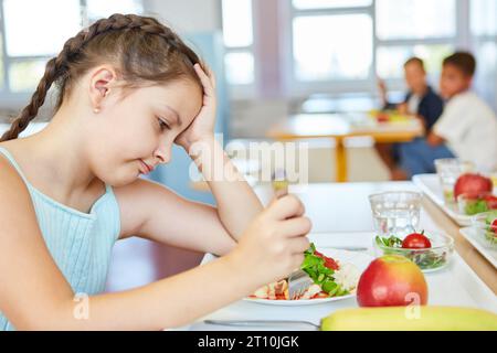 Müdes Mädchen mit Kopf in Hand, das während des Mittagessens in der Schulcafeteria auf den Esstisch starrt Stockfoto
