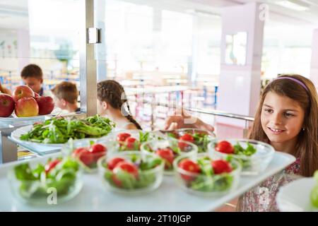 Lächelndes Mädchen, das Gemüsesalat während der Mittagspause im Schulcafé sammelt Stockfoto