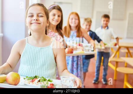 Lächelnde Schülerinnen, die in der Schlange stehen und in der Mittagspause in der Schulcafeteria Essen halten Stockfoto