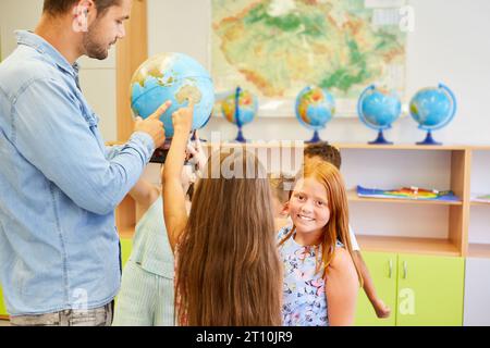 Porträt lächelnder Schulkinder, die mit einem Lehrer stehen, der einen Globus im Geographiekurs hält Stockfoto