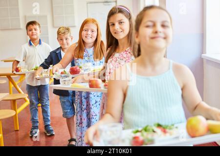 Porträt lächelnder Kinder mit Essenstabletts, die während des Mittagessens in der Schulcafeteria stehen Stockfoto