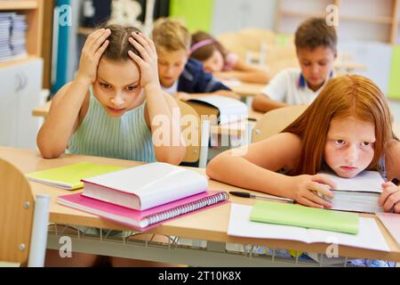 Besorgte Schülerinnen sitzen zusammen auf der Bank mit Büchern im Klassenzimmer Stockfoto