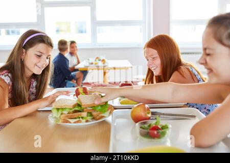 Glückliche Schülerinnen, die während des Mittagessens in der Schule in der Cafeteria frische Sandwiches vom Tisch holen Stockfoto