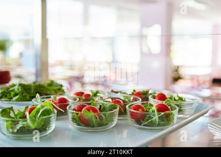 Schüsseln mit frischem Gemüsesalat auf Tablett in der Schulcafeteria Stockfoto