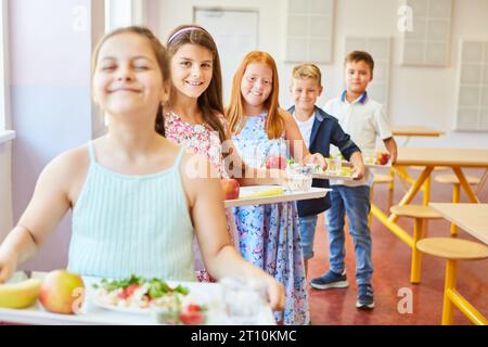 Porträt lächelnder männlicher und weiblicher Schüler, die in der Mittagspause in der Schulcafeteria in der Schlange stehen und Essensschalen halten Stockfoto