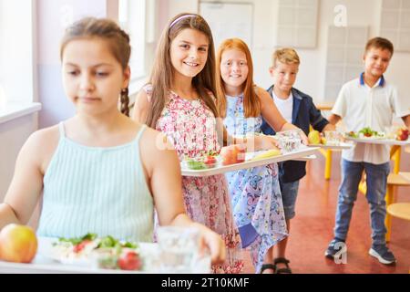 Porträt lächelnder Schülerinnen und Schüler mit Essensschalen, die während der Mittagspause in der Schulcafeteria anstehen Stockfoto