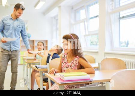 Lächelnde Schülerin, die im Klassenzimmer mit Büchern auf der Bank sitzt Stockfoto