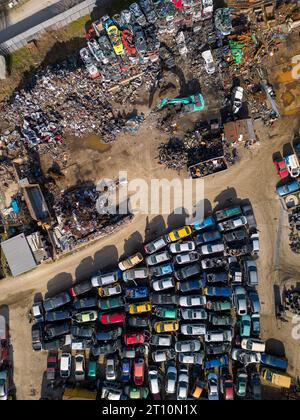 Luftaufnahme einer Autokippe, bei der eine Maschine alte Autos in Schrott zerlegt. Die riesige Sammlung verlassener Autos und die schweren Maschinen, die wir haben Stockfoto