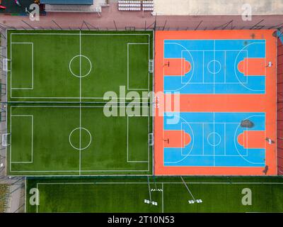 Aus der Vogelperspektive auf ein grünes Fußballfeld und einen farbenfrohen Basketballplatz, der einen Blick auf zwei verschiedene Sporteinrichtungen nebeneinander bietet. Das Gegenteil Stockfoto
