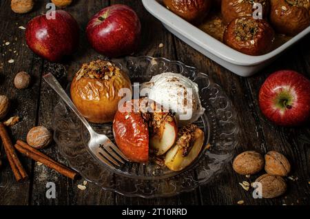 Gefüllte gebackene Äpfel mit Muskatnuss, Walnüssen, Zimt und Honig, serviert mit Eis auf dunkler Holzoberfläche Stockfoto