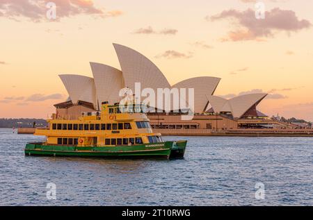 Das Opernhaus von Sydney bei Sonnenuntergang mit einer Fähre von Sydney, die am Hafen von Sydney vorbeifährt, Sydney, New South Wales, Australien Stockfoto