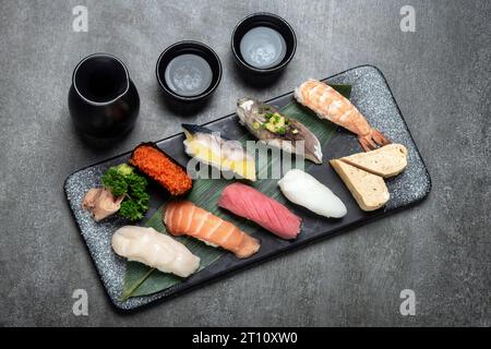 omakase gemischtes Sushi-Set mit Sake auf grauem Hintergrund im japanischen Restaurant Stockfoto