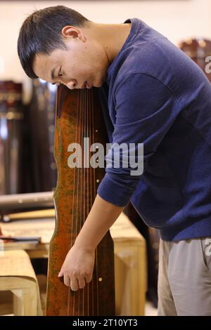 (231010) -- KAIFENG, 10. Oktober 2023 (Xinhua) -- Guqin-Produzent Xu Yachong spielt das Guqin im Lankao County der Stadt Kaifeng, Zentralchinas Provinz Henan, 9. Oktober 2023. Lankao County ist reich an Paulownia-Bäumen, ein idealer Rohstoff für die Herstellung von Musikinstrumenten. Doch im letzten Jahrhundert führten häufige Überschwemmungen und Sandstürme zu schlechten Böden und Ernteausfällen. In den 60er Jahren initiierte der lokale Parteichef Jiao Yulu die Einheimischen, Paulownia-Bäume zu Pflanzen, um den Boden zu verbessern und Wasser zu sparen. In den 1980er Jahren, als die Bäume blühten, fanden die Einheimischen das feine Material, um Möbel herzustellen. Stockfoto