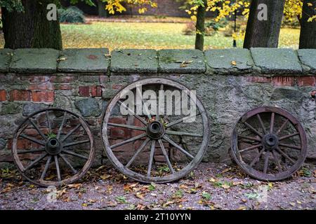 Drei alte Holzräder stehen an einer Mauer, im Hintergrund der Park der Burg. Stockfoto